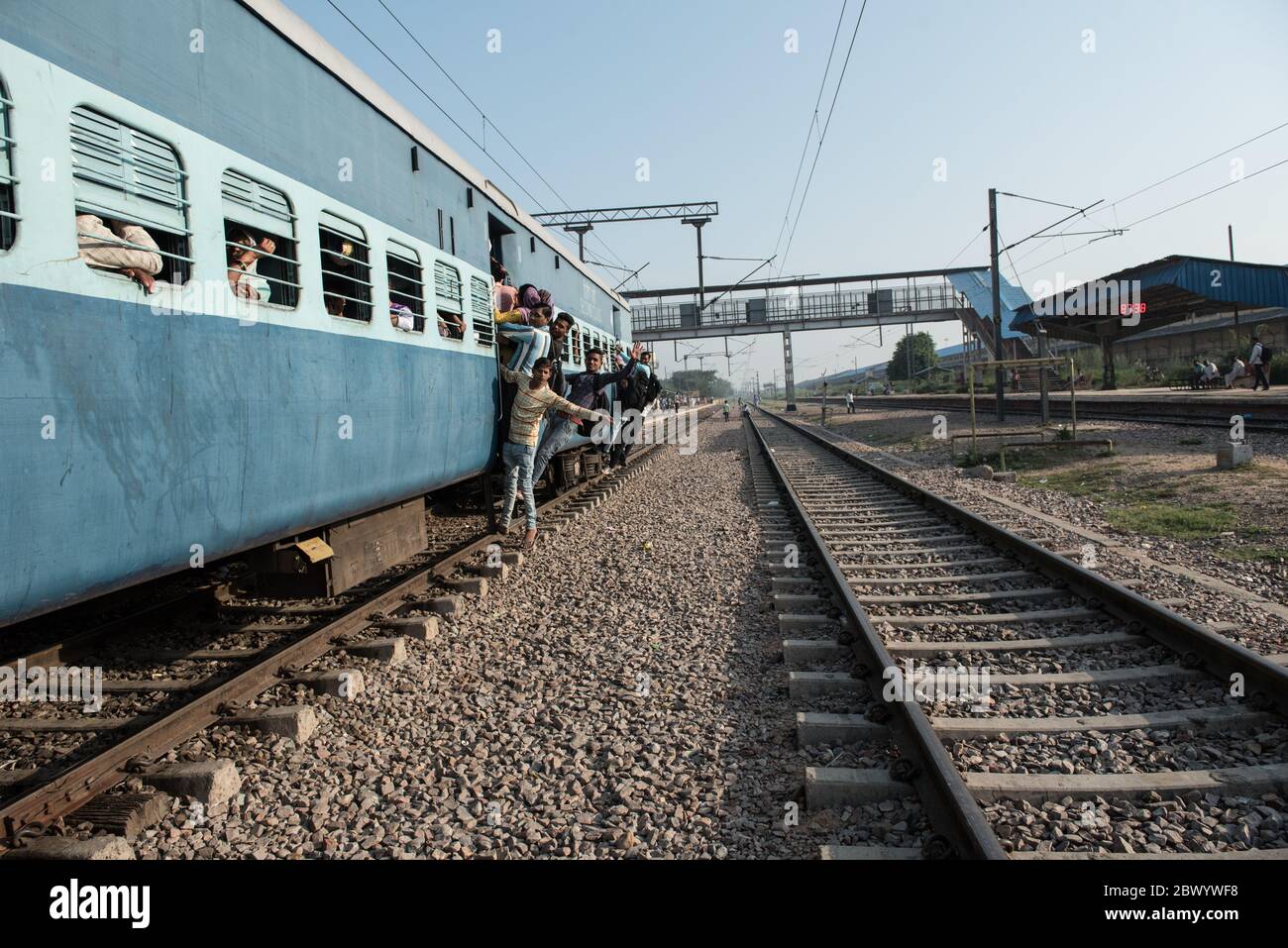 Commuters hang out of an overcrowded Indian Railways train, at Noli Railway Station near