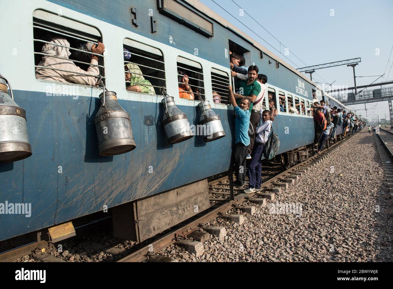 Commuters hang out of an overcrowded Indian Railways train, at Noli Railway Station near