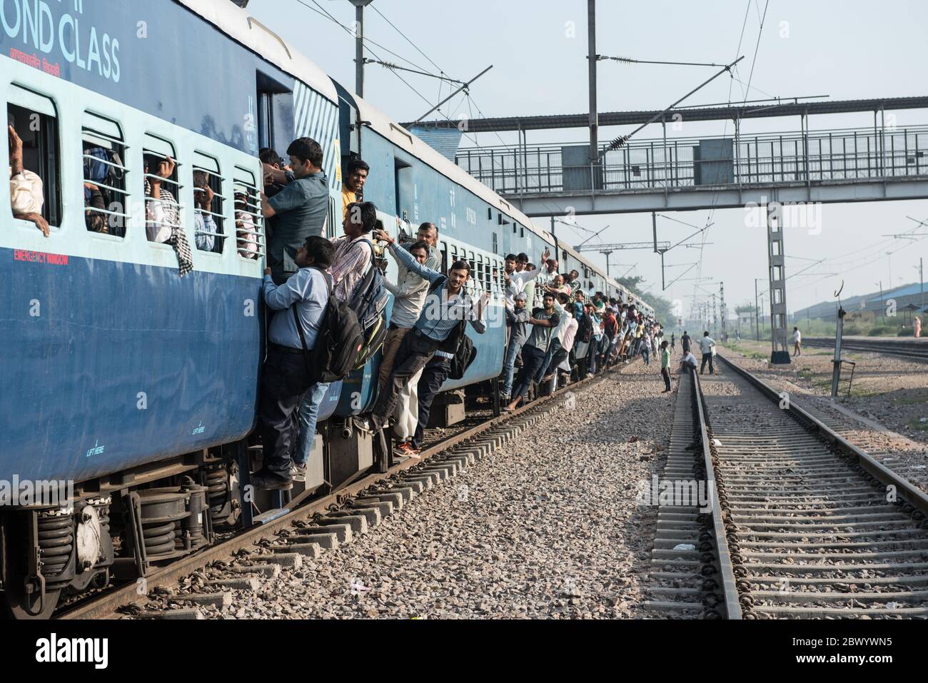Commuters hang out of an overcrowded Indian Railways train, at Noli Railway Station near Ghaziabad, New Delhi, India. Stock Photo