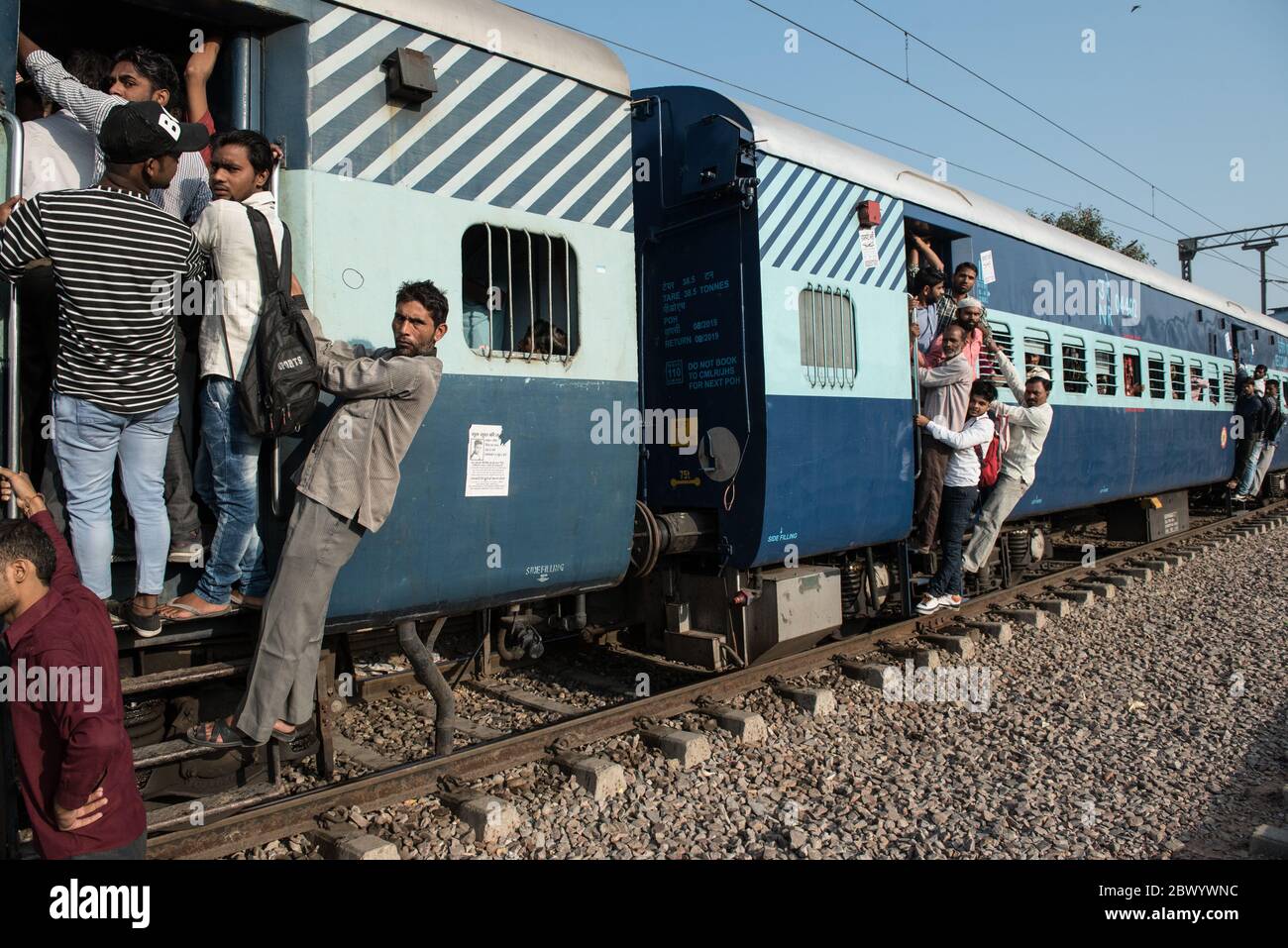 Commuters hang out of an overcrowded Indian Railways train, at Noli Railway Station near