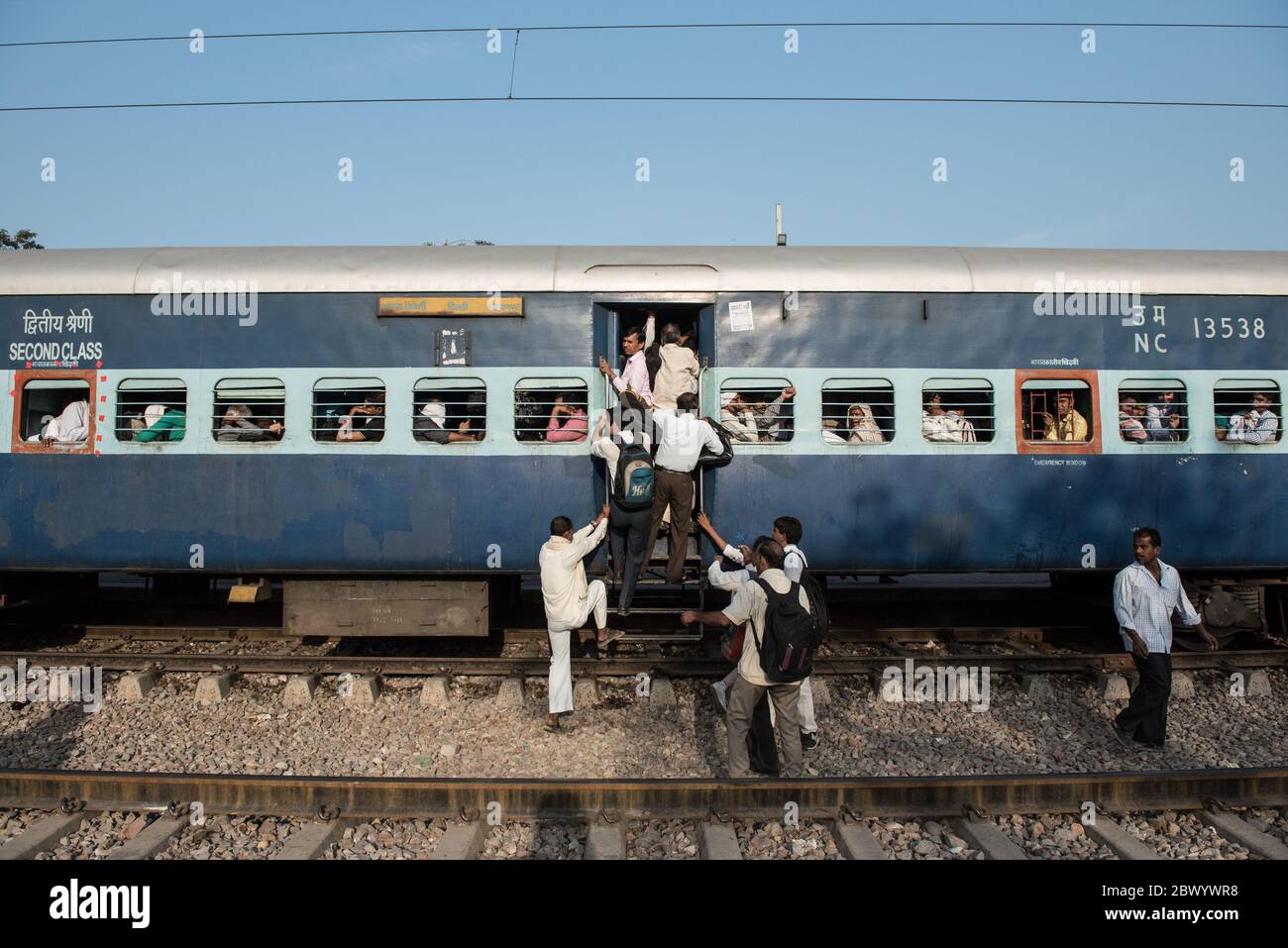 Commuters hang out of an overcrowded Indian Railways train, at Noli Railway Station near