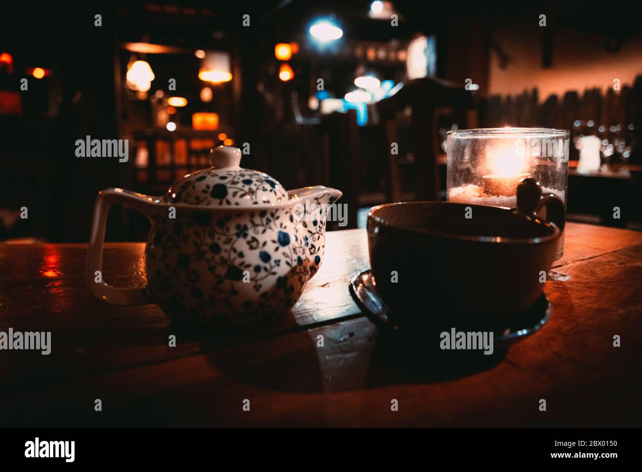 A teapot, a cup and a tealight inside a glass over a wooden table of a