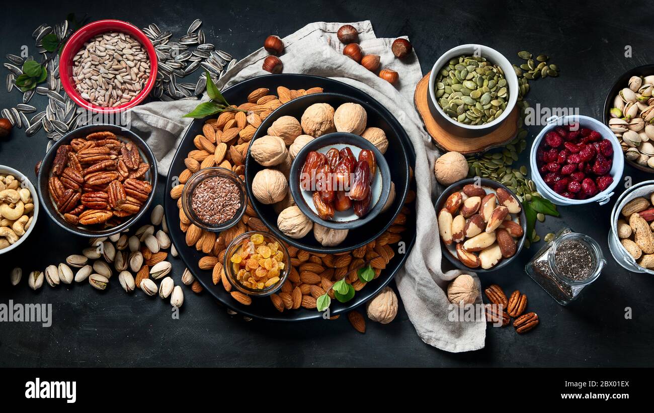 Different types of nuts, seeds and dried fruits on black background
