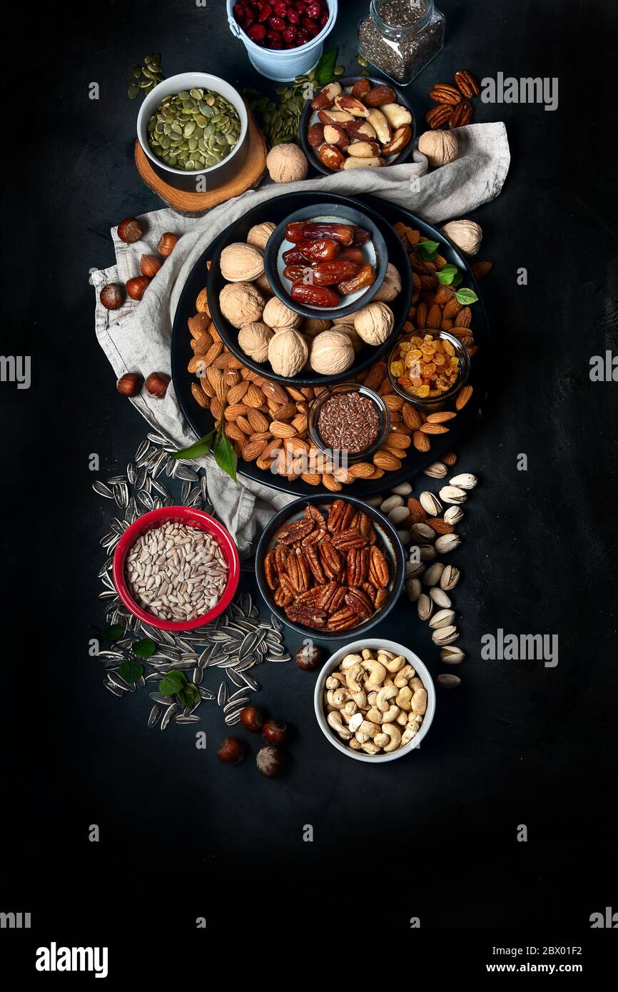 Different types of nuts, seeds and dried fruits on black background