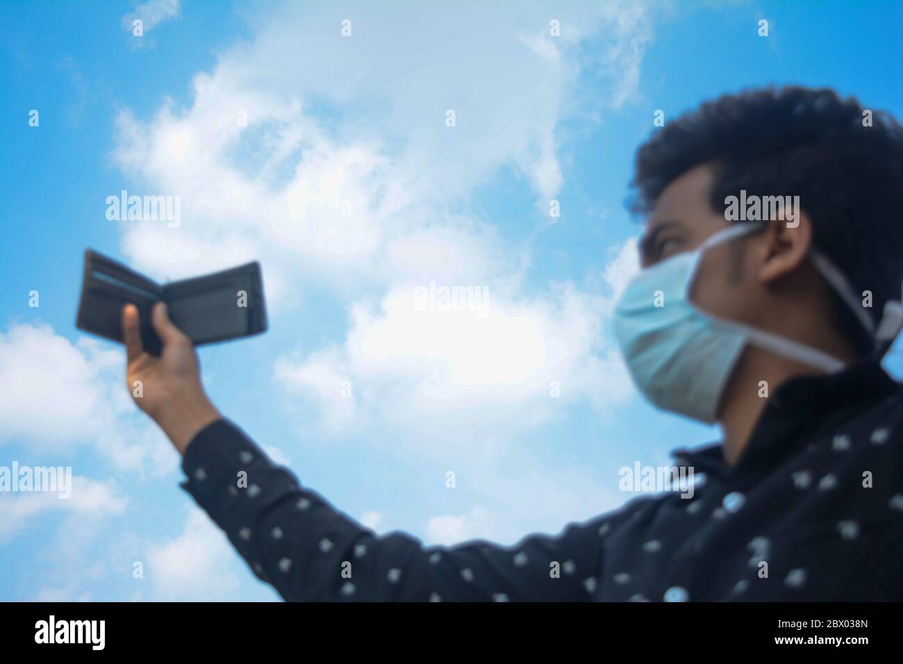 Man wearing face mask and showing his wallet on blue sky background.selective focus on sky. Stock Photo