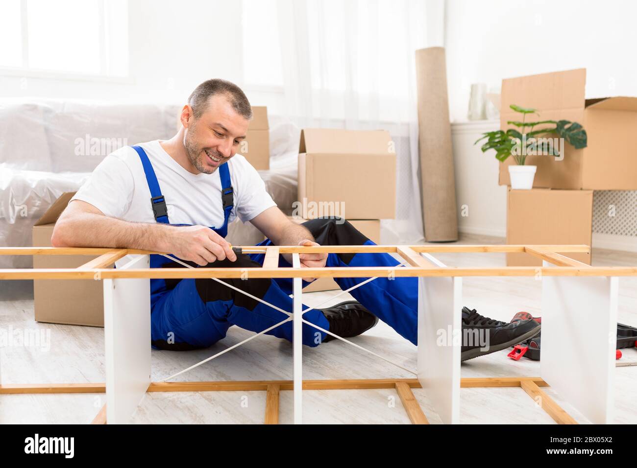 Happy Furniture Assembler In Blue Coverall Fixing Shelf Indoor Stock Photo