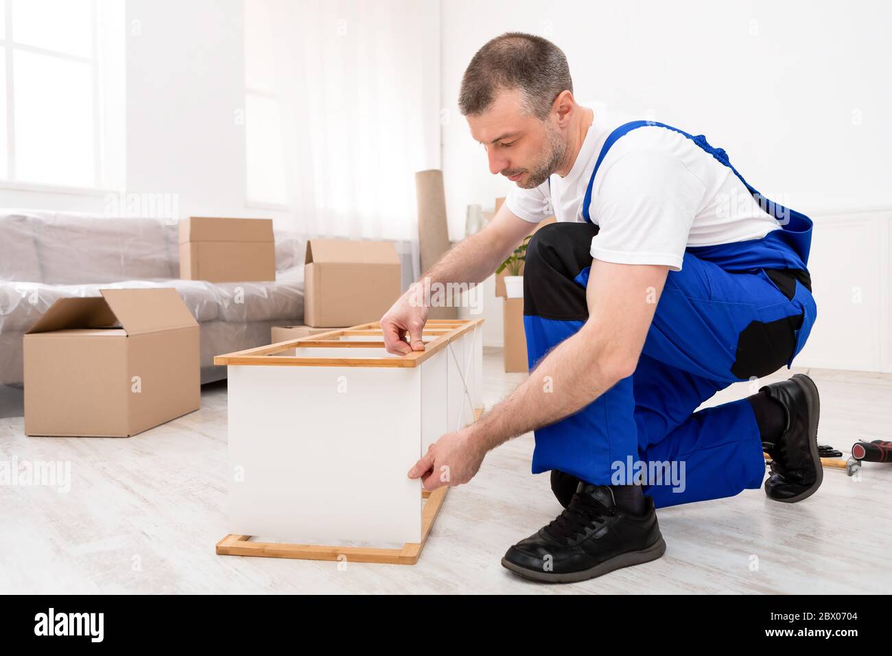 Repairman Assembling Furniture In Flat After Relocation, Wearing Blue Coverall Stock Photo