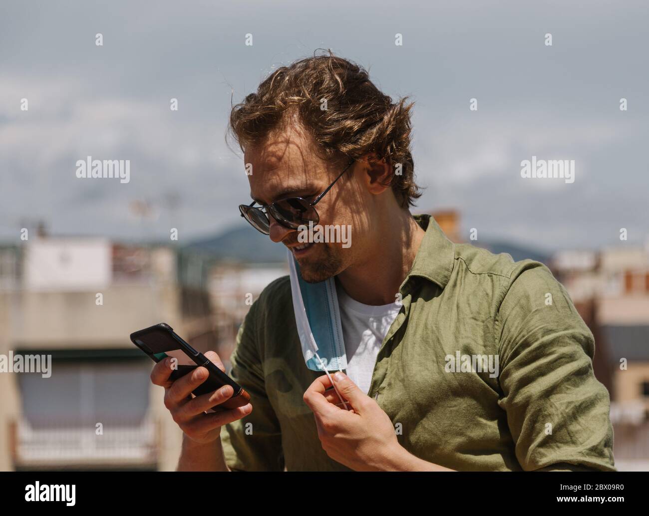 Smiling european man taking off protective mask to unblock the phone. The man is happy to be free and meet with friends. Stock Photo