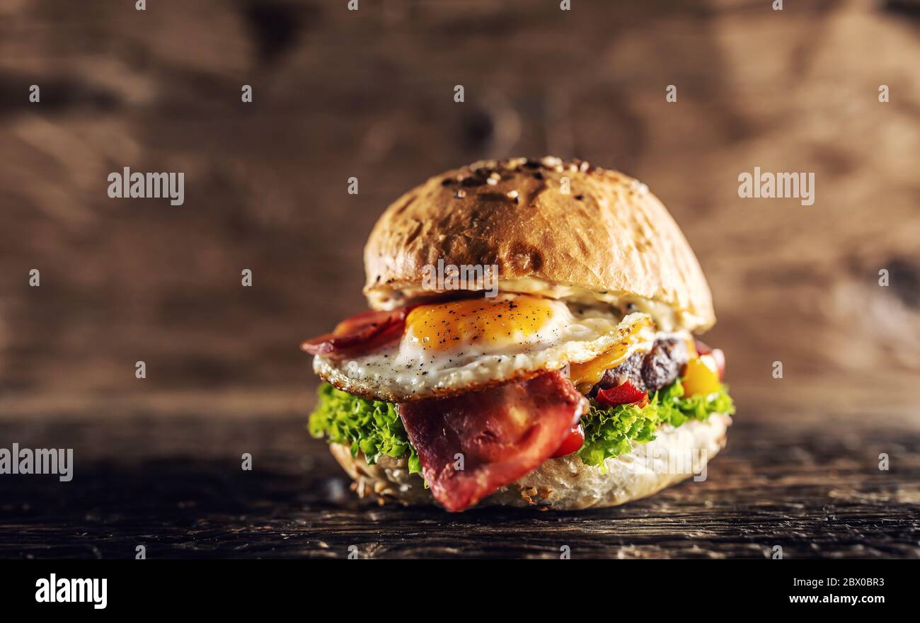 Beef burger with melted cheese, egg, bacon and veg on a rustic table Stock Photo