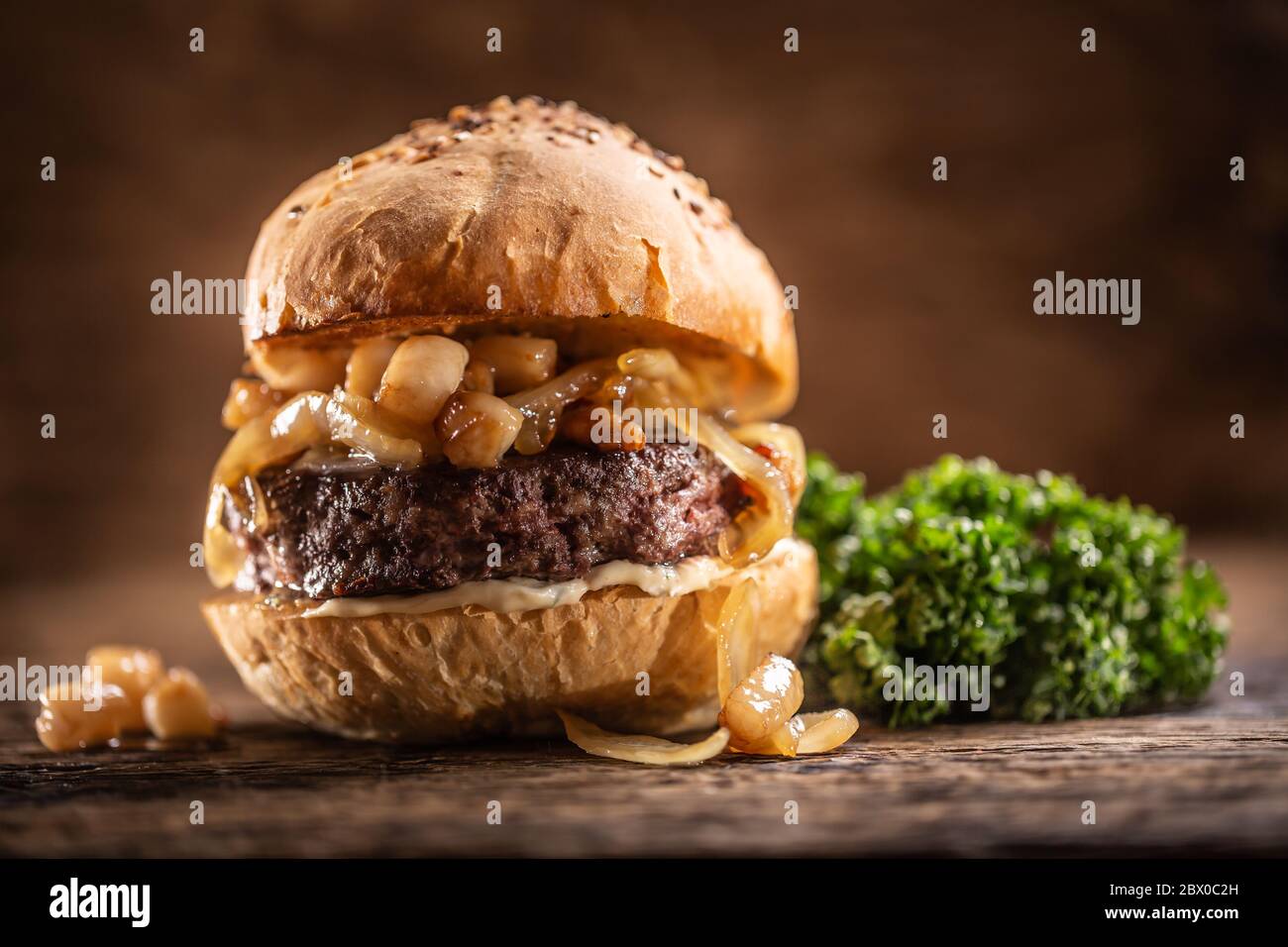 Beef burger with melted cheese, caramelized onions in a sesame bun with salad on the side Stock Photo