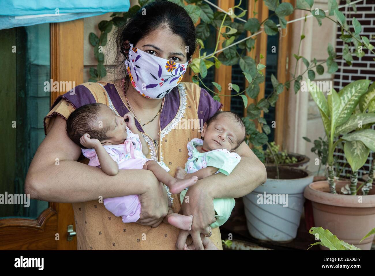 Young Mother Wearing Mask Holding Her Two Newborn Twin Babies, Stay Home Taking Extra Care Due