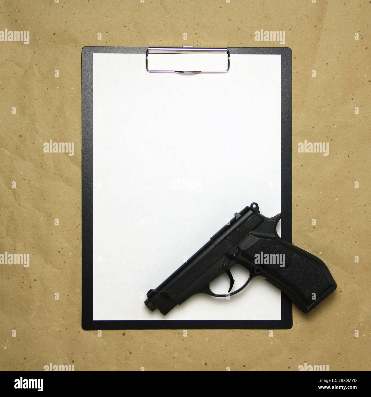 A tablet with a white sheet of A4 format with gun on a beige craft paper. Concept of the legal system, criminal organizations, security services. Stock photo with empty place for your text and design. Stock Photo