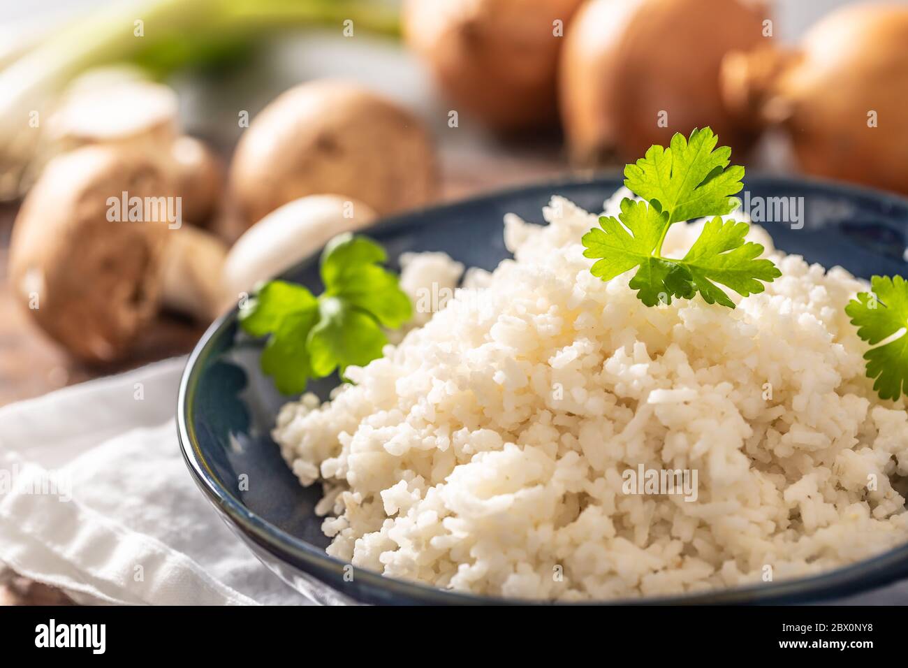 Bowl of steamed rice and parsley tops with mushrooms and leaks in the background Stock Photo