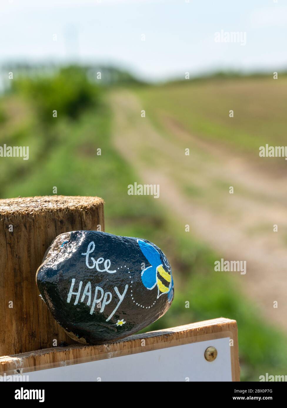 'Bee Happy' painted stone on gatepost by countryside footpath in Leicestershire during Covid-19 lock-down, England, UK Stock Photo