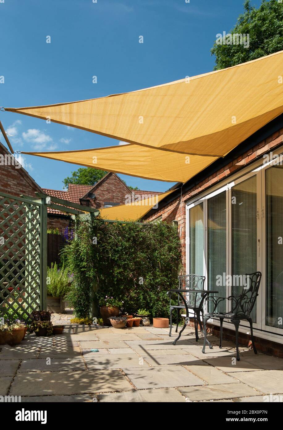 https://c8.alamy.com/comp/2BX0P7N/small-garden-patio-with-yellow-triangular-sail-shade-sunshades-and-blue-sky-above-on-a-sunny-summer-day-england-uk-2BX0P7N.jpg