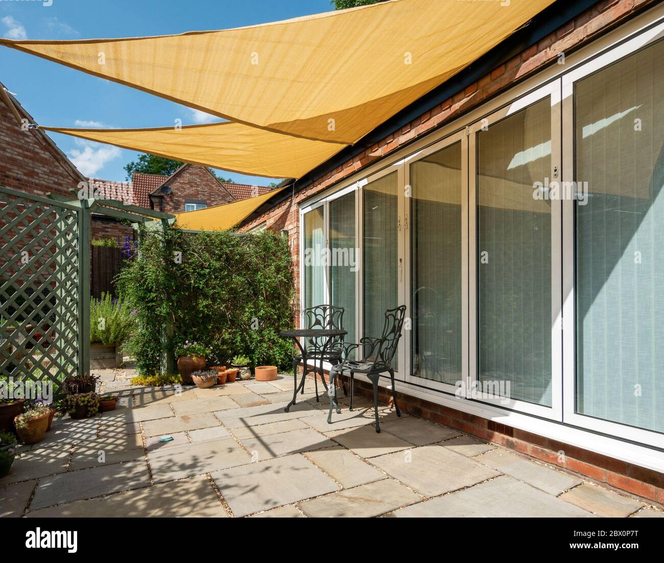 Small garden patio with yellow, triangular sail shade sunshades and blue sky above on a sunny Summer day, England, UK Stock Photo