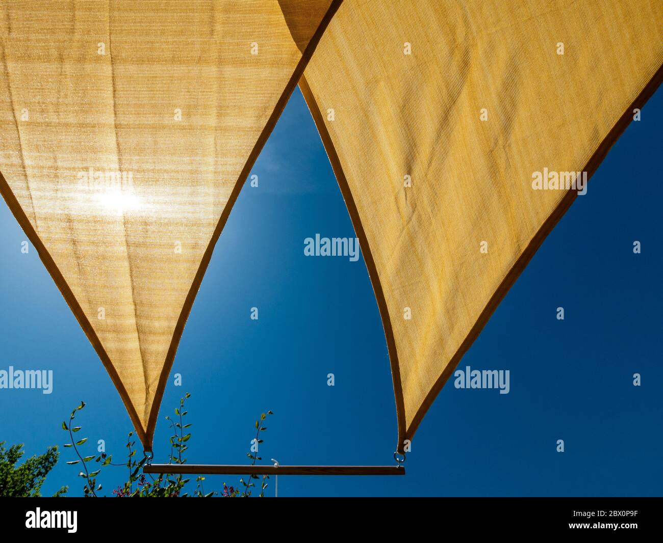 Looking up at sun shining through two triangular sail shade sunshades with blue sky on a sunny Summer day, UK. Stock Photo