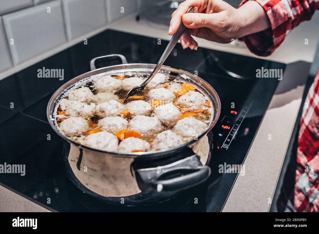 Spooning the soup with a spoon while cooking on an induction cooker in