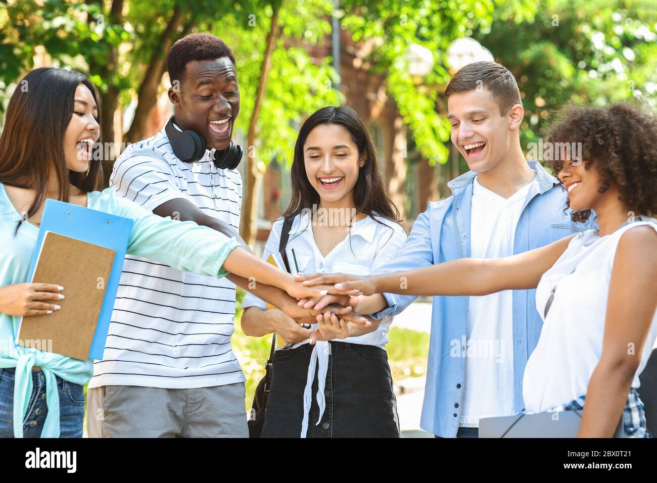 Group Of University Friends Stacking Hands Outdoors After Successful Exams Pass Stock Photo