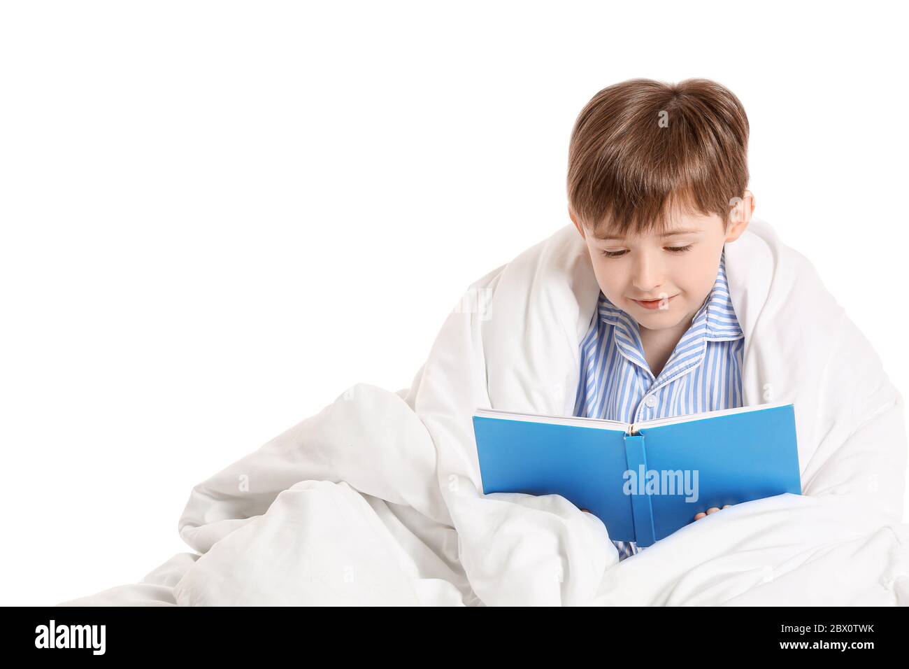 Little boy wrapped in blanket reading book on white background Stock