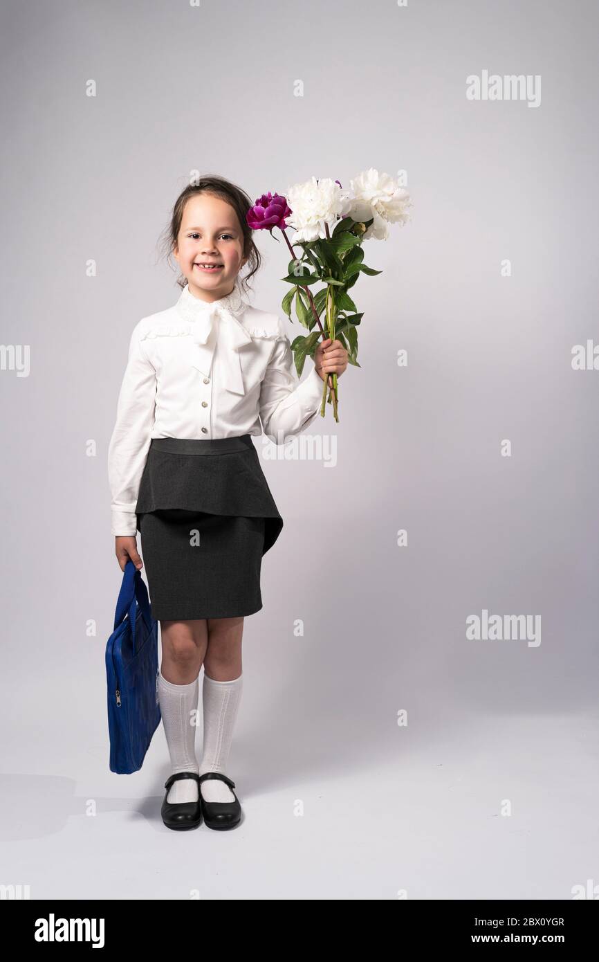 first grade school girl in a white shirt holding flowers and a backpack Stock Photo