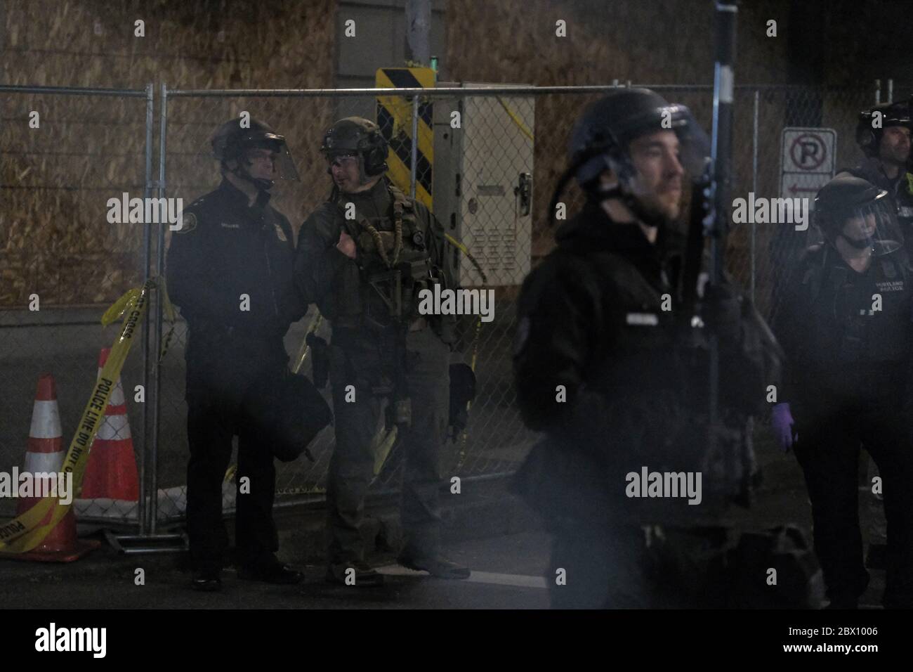 Portland, USA. 04th June, 2020. An armed Special Emergency Response Team ( SERT) officer stands with police behind a fence blocking access to the  Justice Center on the sixth night of action against