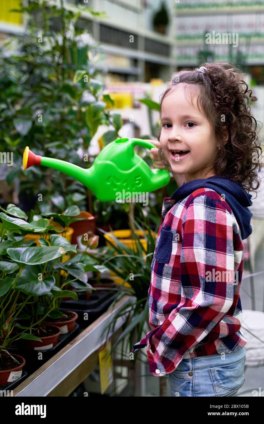 a little curly-haired girl waters her home plants Stock Photo