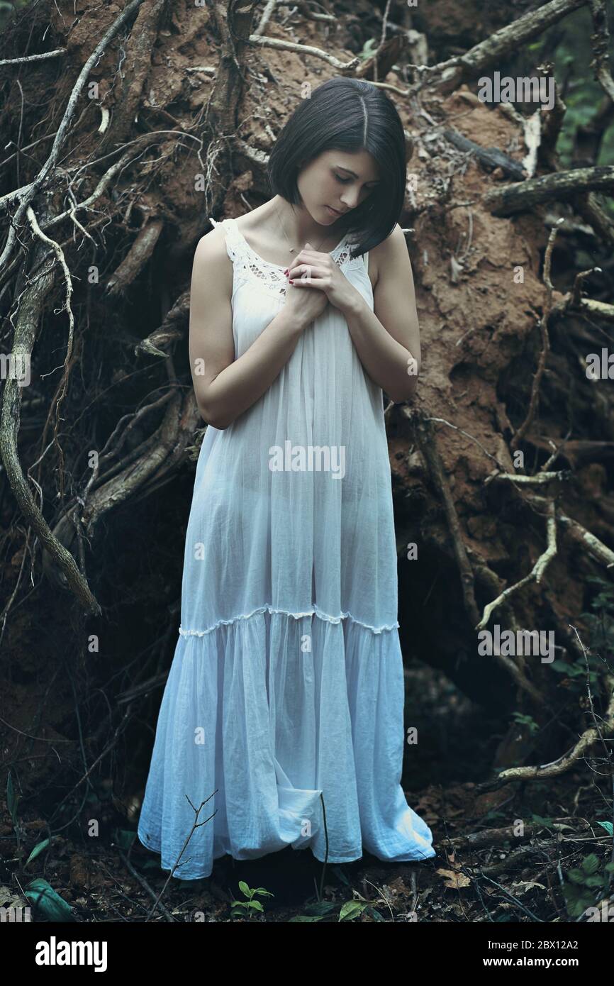 Beautiful woman with eyes closed praying among dead trees . Dark fantasy Stock Photo
