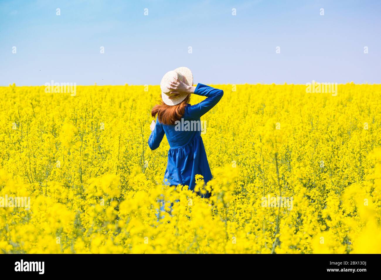 Happy girl in a hat walking in amazing field of yellow rapeseed in the ...