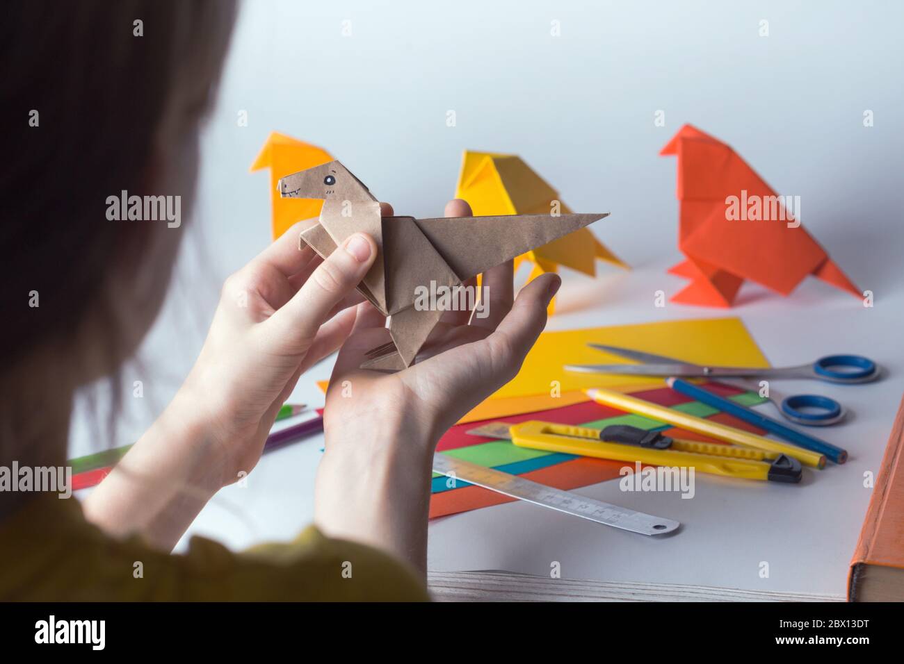 girl makes origami dinosaur of colored paper. paper, ruler, pencils, knife. interesting hobby Stock Photo