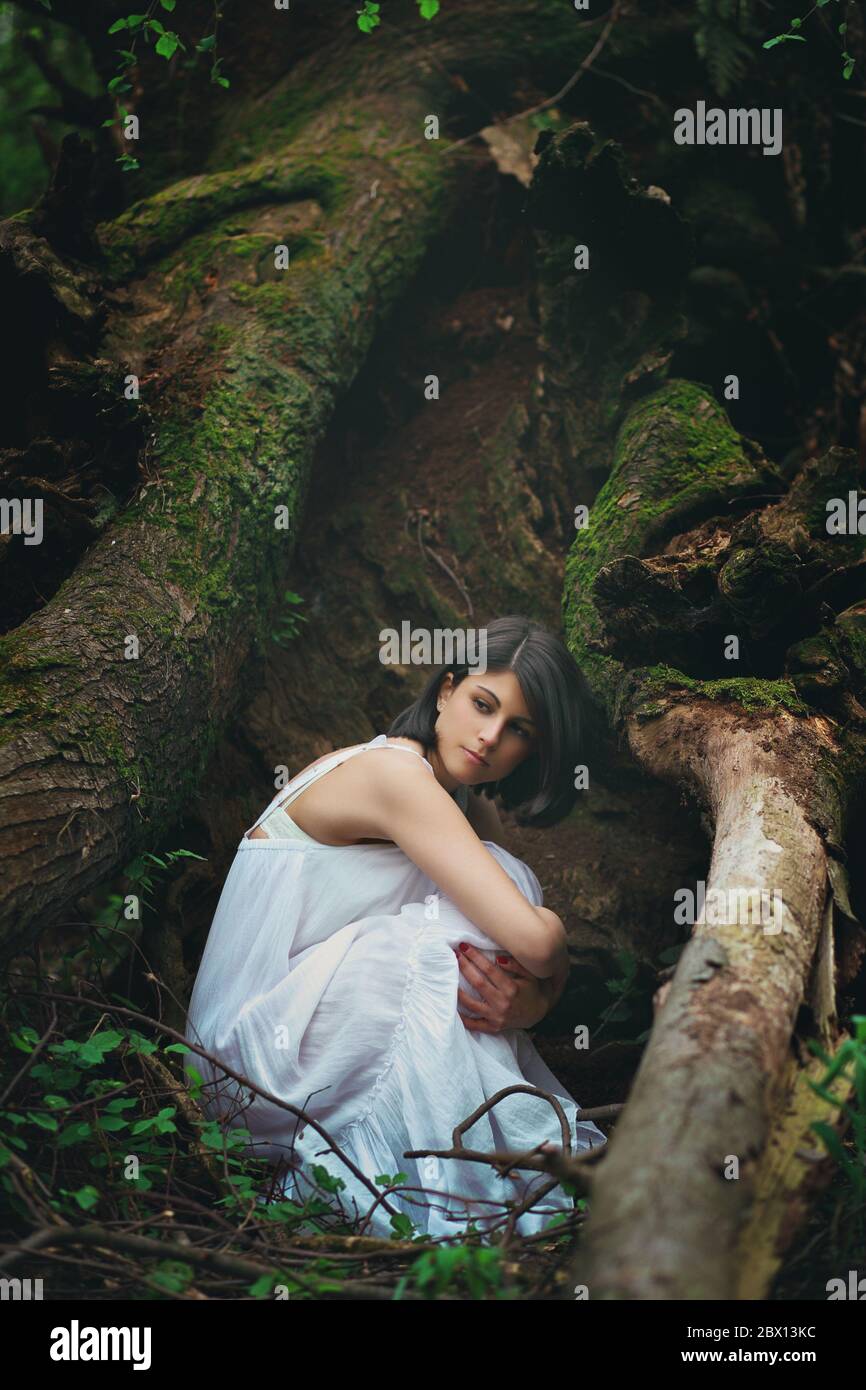 Romantic portrait of a beautiful woman among dark tree roots. Mother earth embrace Stock Photo