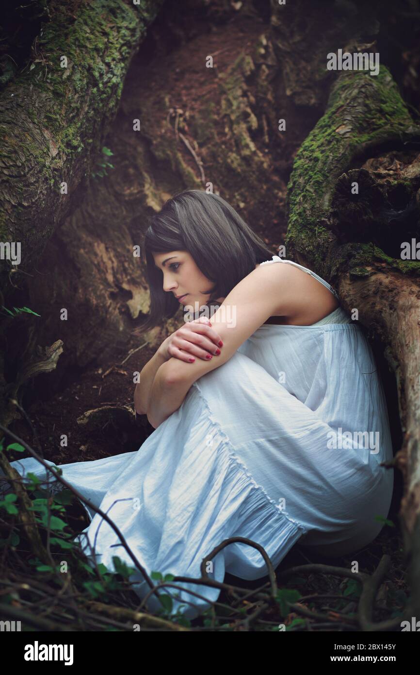 Thoughtful woman among dark tree roots . Mother earth embrace Stock Photo