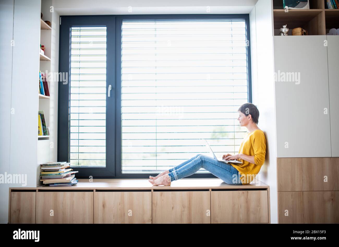 Young woman with laptop sitting on window sill in bedroom indoors at ...