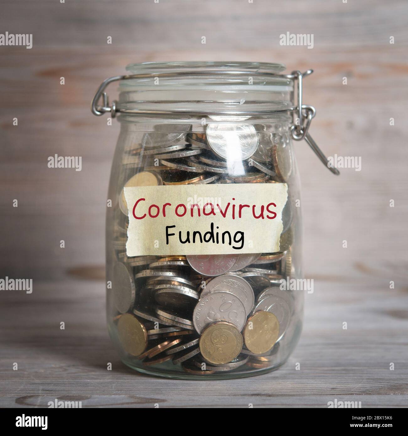 Coins in glass money jar with Coronavirus Funding label, financial concept. Vintage wooden background with dramatic light. Stock Photo
