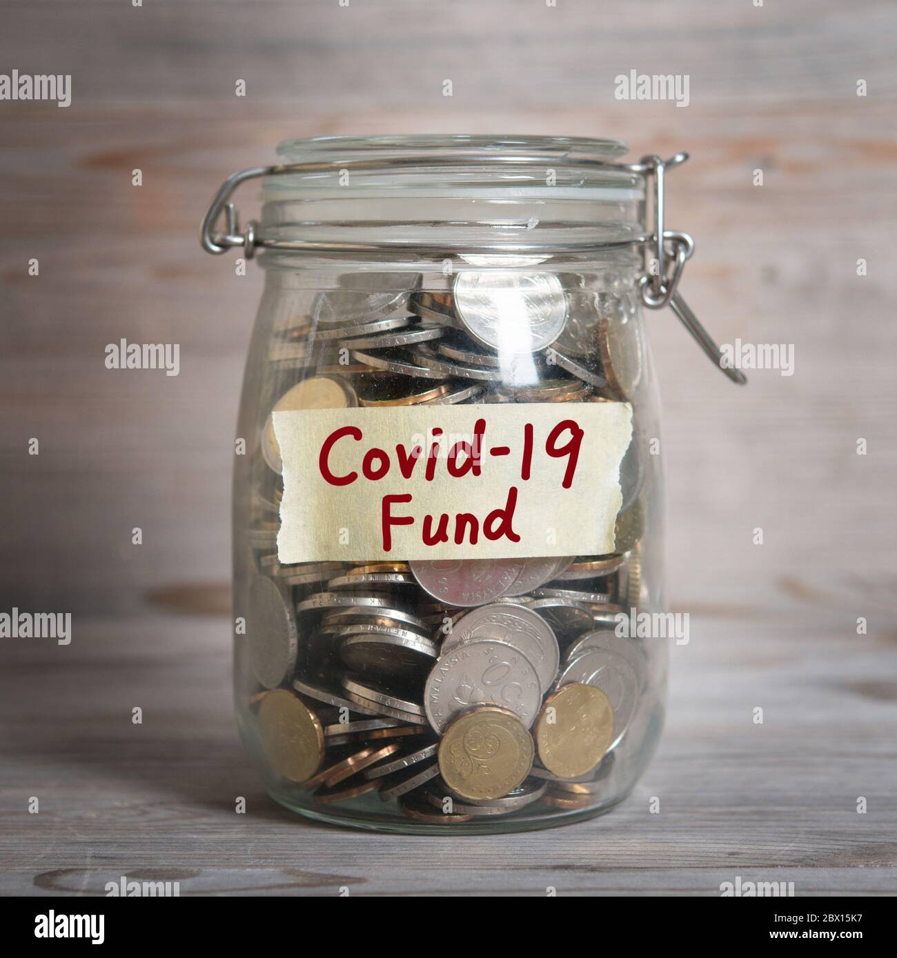 Coins in glass money jar with covid19 fund label. Vintage wooden background with dramatic light. Stock Photo