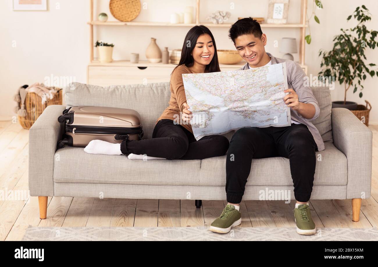 Asian Couple Holding World Map Sitting On Couch At Home Stock Photo