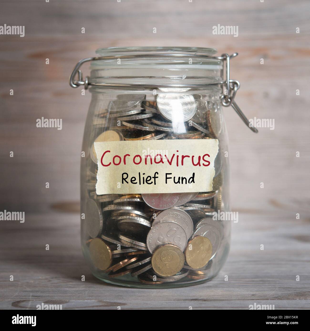 Coins in glass money jar with Coronavirus relief fund label, financial concept. Vintage wooden background with dramatic light. Stock Photo
