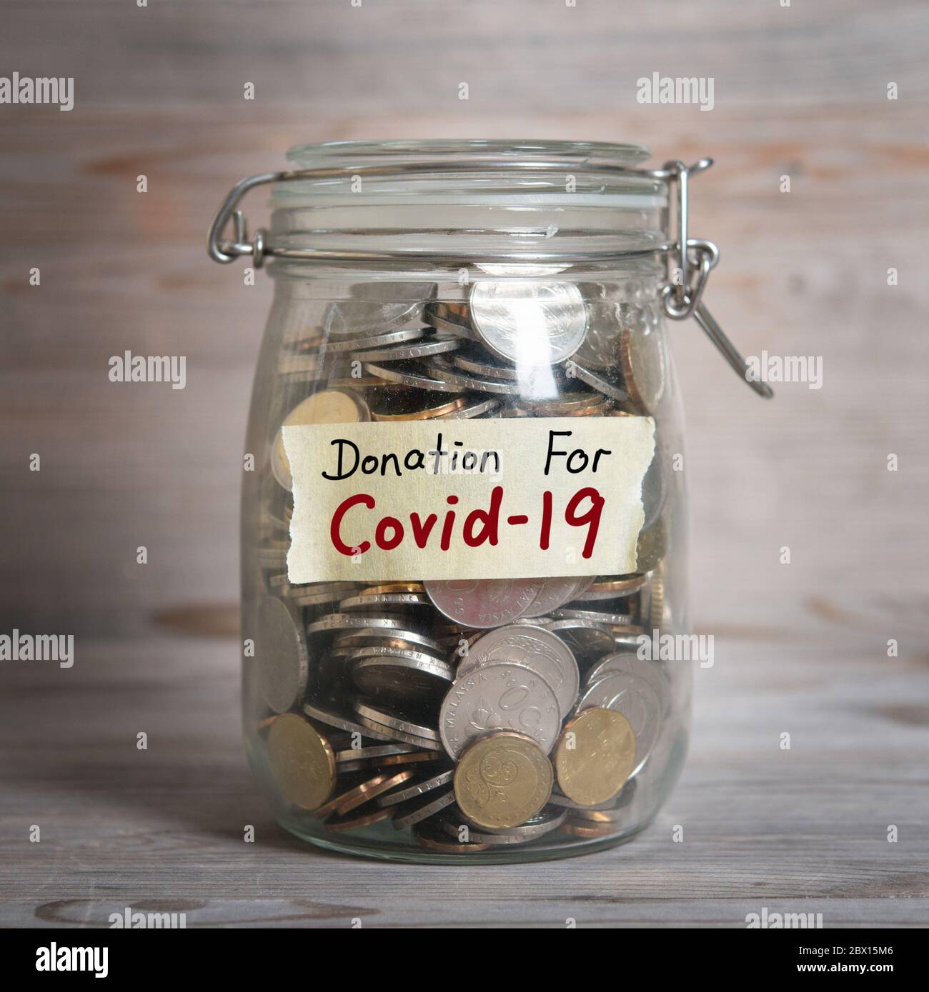 Coins in glass money jar with donation for covid19 label, financial concept. Vintage wooden background with dramatic light. Stock Photo