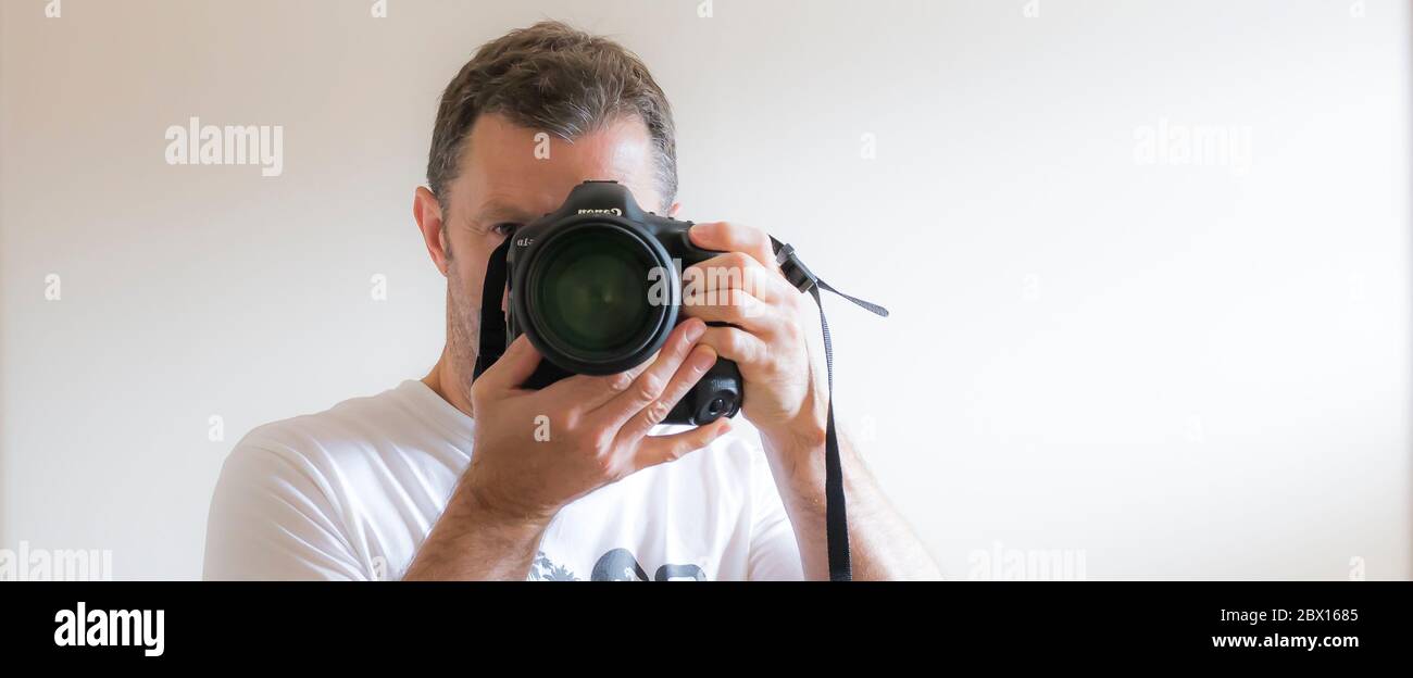 Close up isolated UK male photographer taking photograph of himself, a selfie, in interior mirror using Canon equipment. Taking professional selfie. Stock Photo