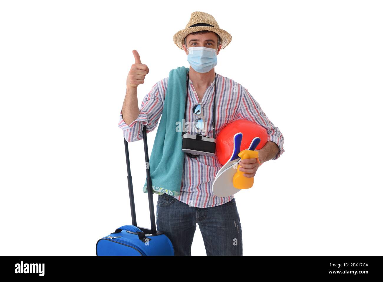 Happy man ready to travel on holiday during the coronavirus season with his thumbs up ok dress for the occasion with beach accessories and suitcase is Stock Photo