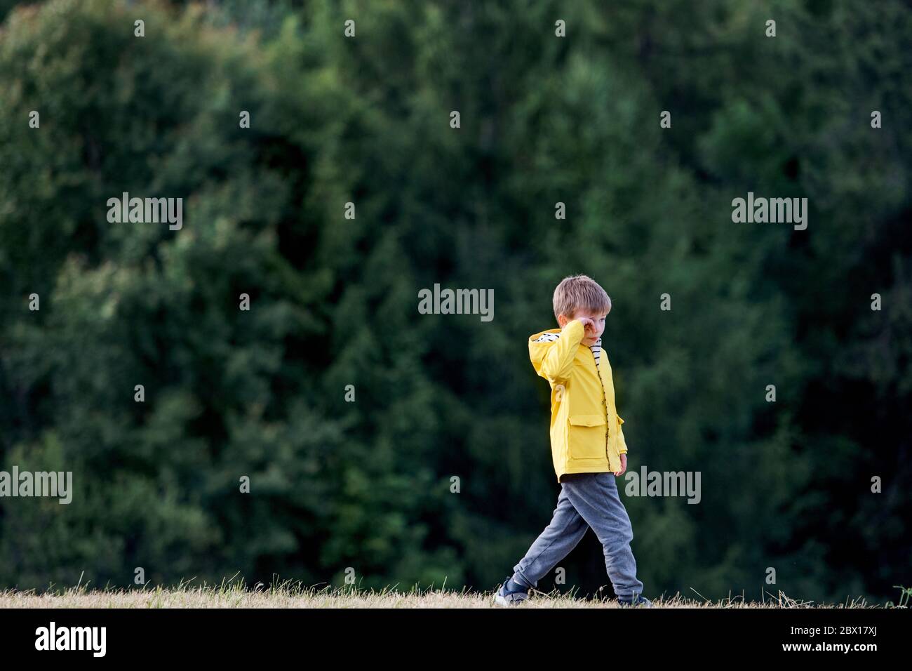 Side view of school child walking on field trip in nature, rubbing eyes. Stock Photo