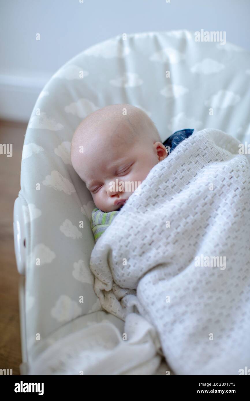 A newborn baby boy sleeping in a baby bouncer  Photo by Sam Mellish Stock Photo
