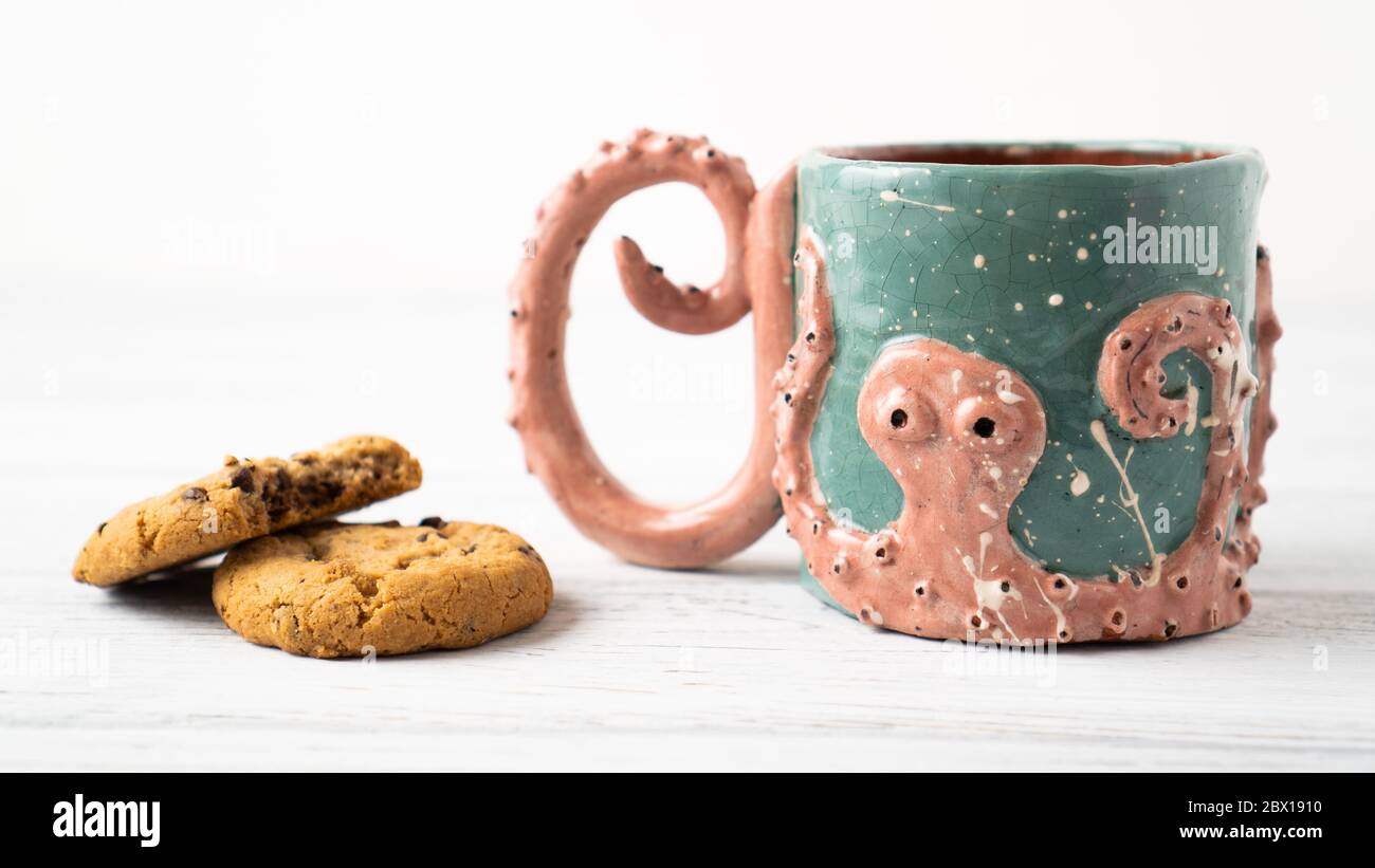 Self made Kraken mug and bitten chocolate chip cookie. Original cup as a gift. Octopus crafts. Personalized mug Stock Photo