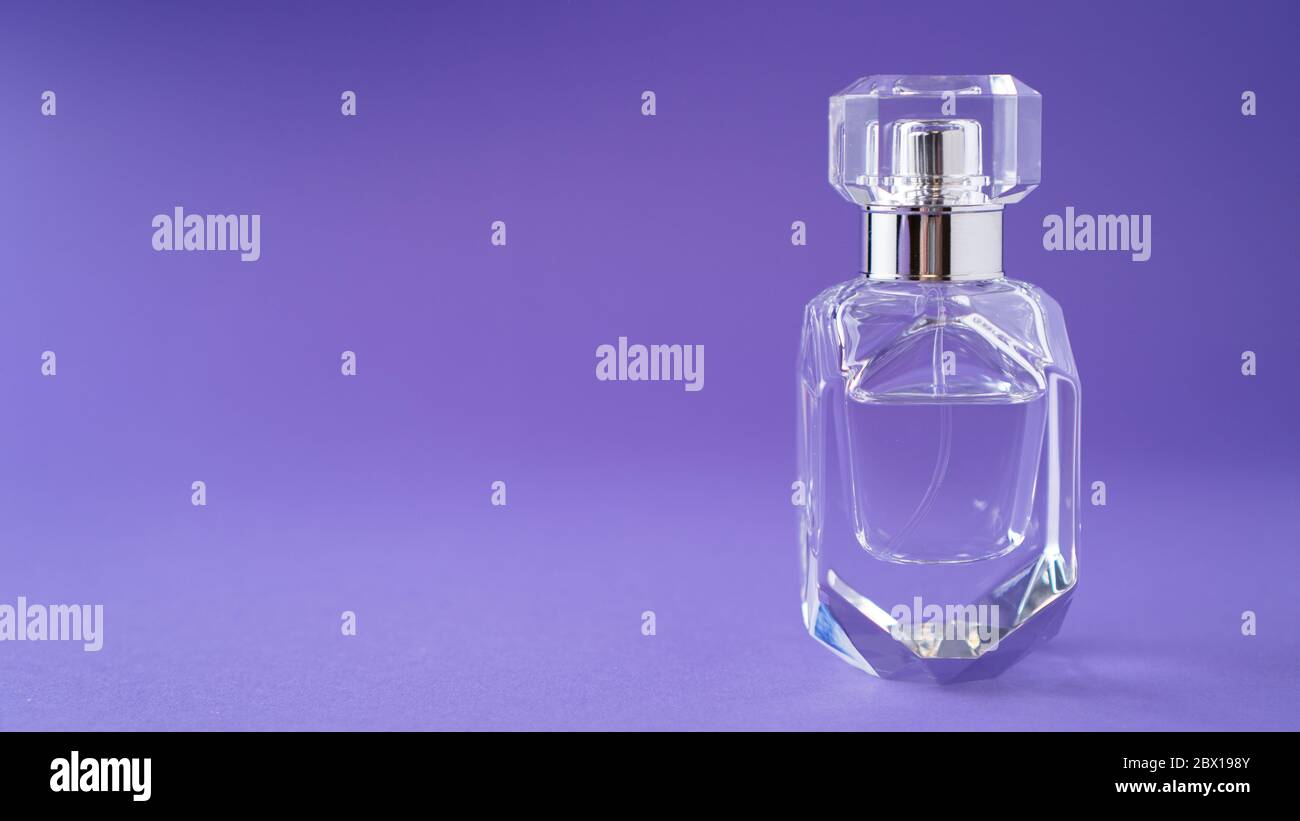 Isolated transparent perfume bottle on purple background. Gift concept. Fragrance spray mock up. Spring scent Stock Photo