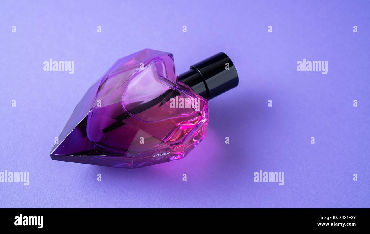 Isolated heart shaped perfume bottle on purple background. Gift concept. Fragrance spray mock up. Romantic scent Stock Photo