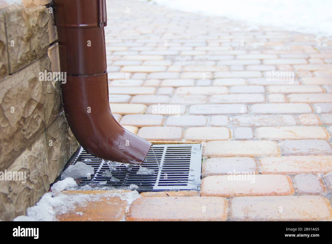 Metal downspout and a storm grate, concept of season change. Closeup with selective focus. Stock Photo