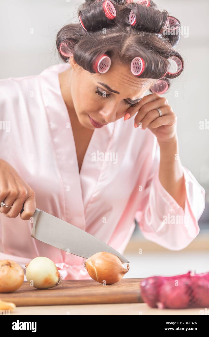 Woman in hair curlers and nighgown cries from onion cutting in the