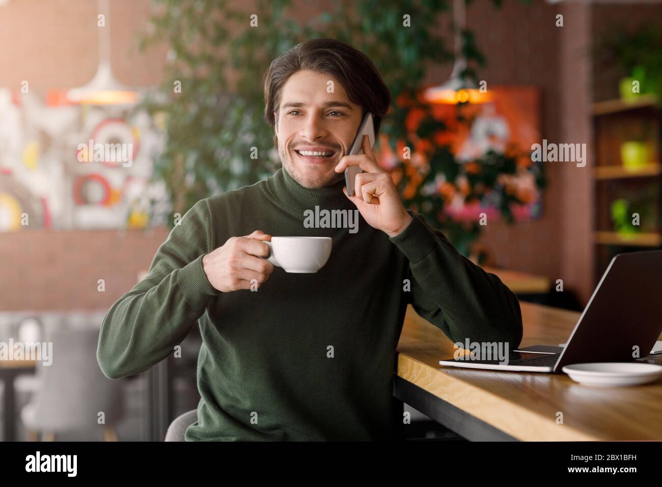 Cheerful young man working with laptop at cafe Stock Photo