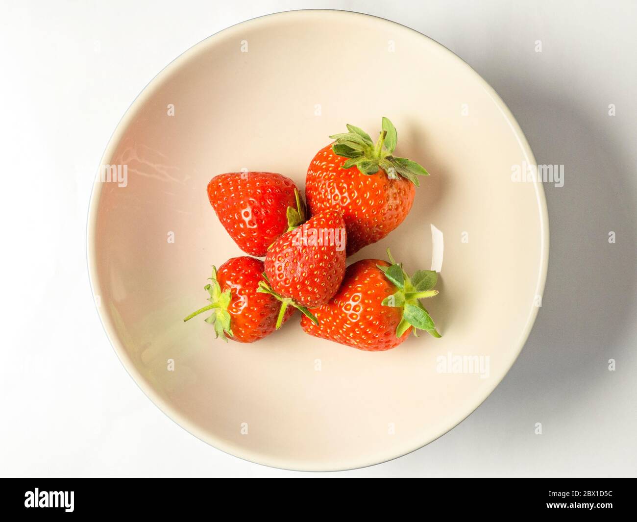 Five fresh strawberries with stalks in a bowl on a white background Stock Photo