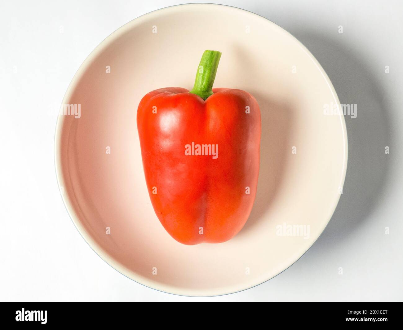 A single red bell pepper in a bowl isolated on a white background Stock Photo